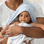 Adorable Black Infant Baby In Towel Relaxing In Father’s Arms After Bath