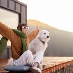 Woman with her dog resting on terrace of tiny house on nature